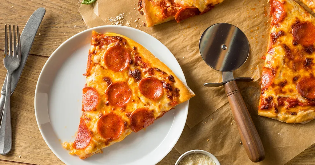 Overhead view of pepperoni pizza with a slice served on a plate